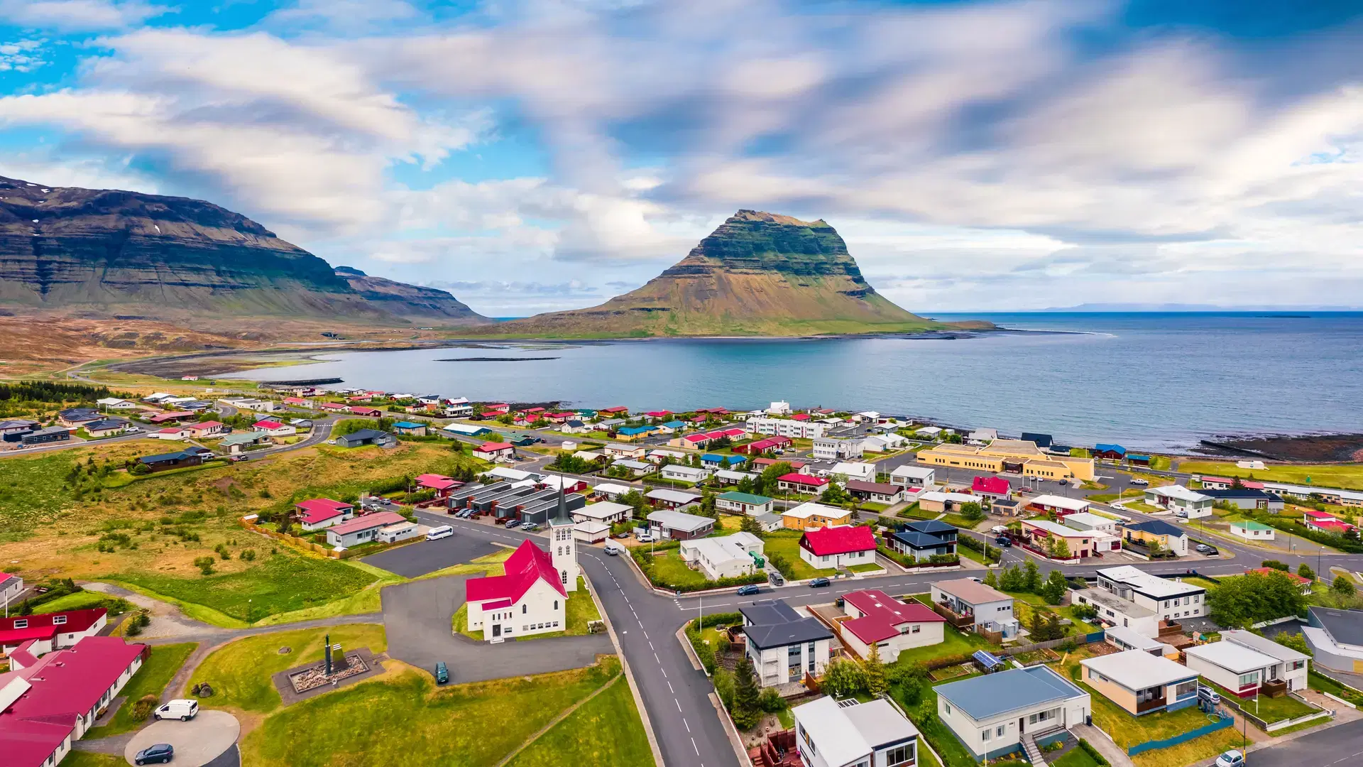 View from flying drone. Amazing morning cityscape of Grundarfjordur town with Kirkjufell Mountain on background. Aerial view of Grundarfjordur Church, Iceland, Europe. Traveling concept background. 