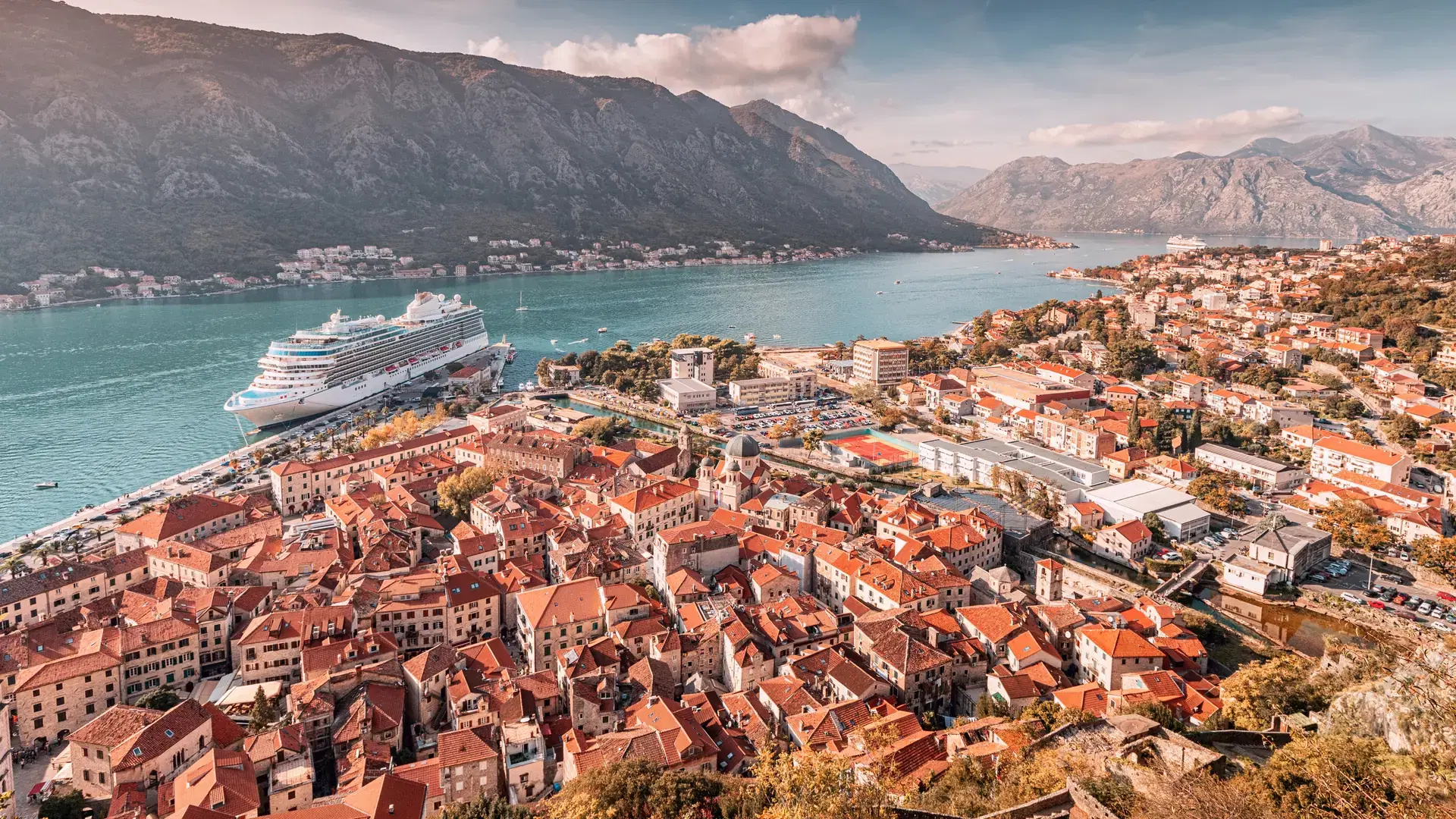 Aerial view of Kotor old town with orange rooftops and cruise ship in bay, at Montenegro, in beautiful autumn sunlight