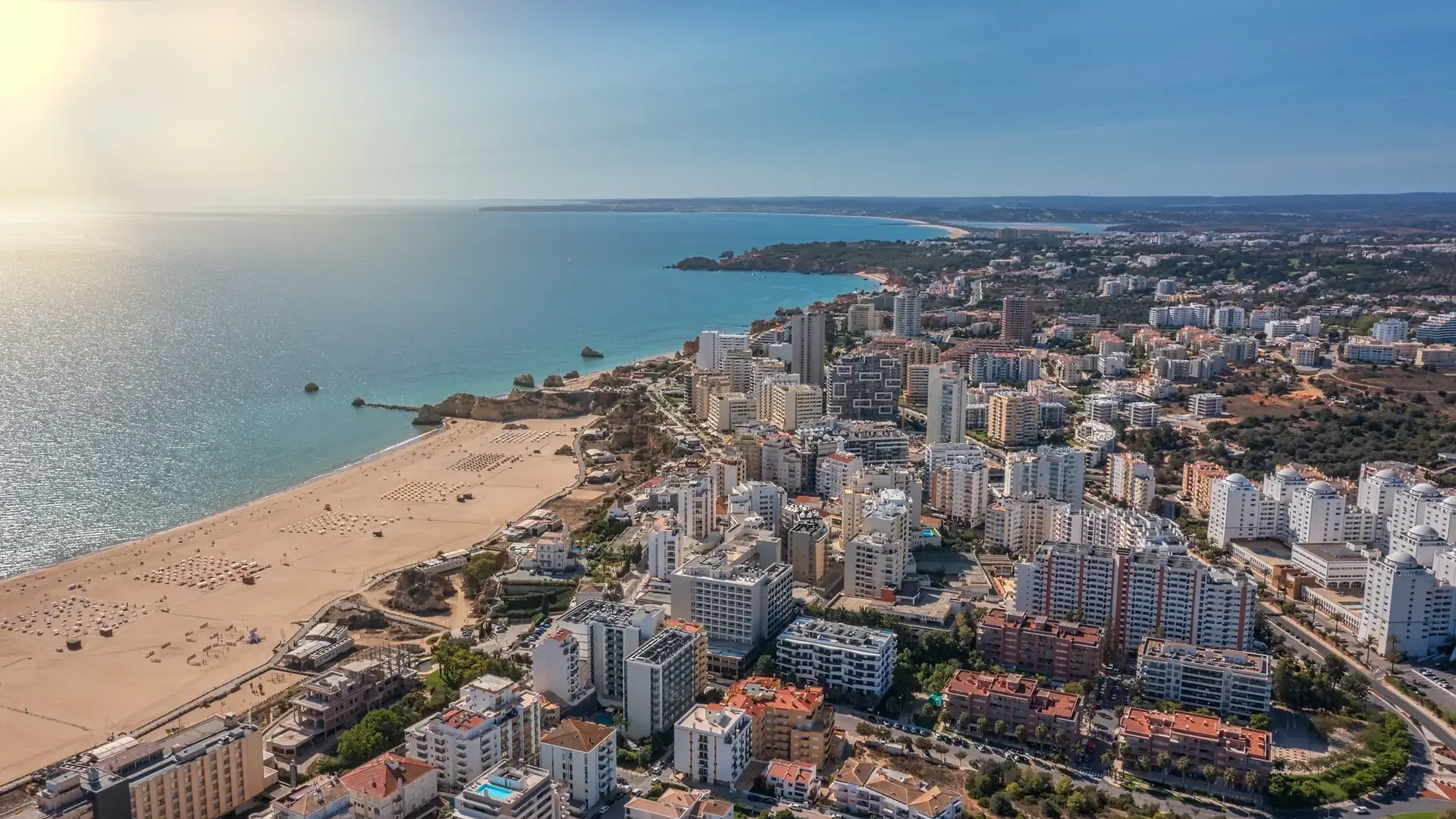 Aerial view of the city of Portimao over residential buildings, high-rise buildings, on the beach Praia de Rocha with tourists. Sunny day