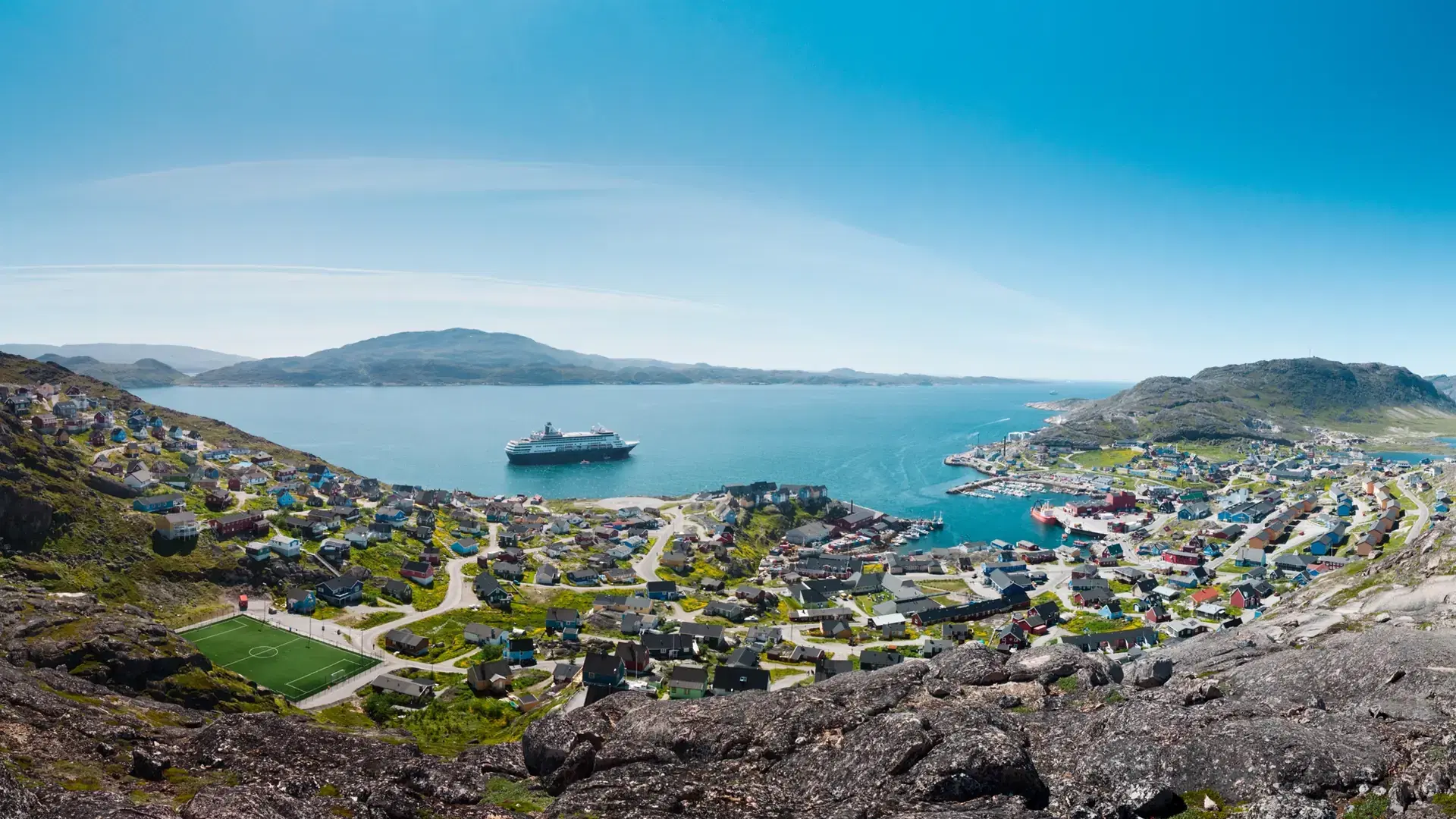 A panoramic shot of the coast at Greenland, Qaqortoq with a boat sailing in the sea