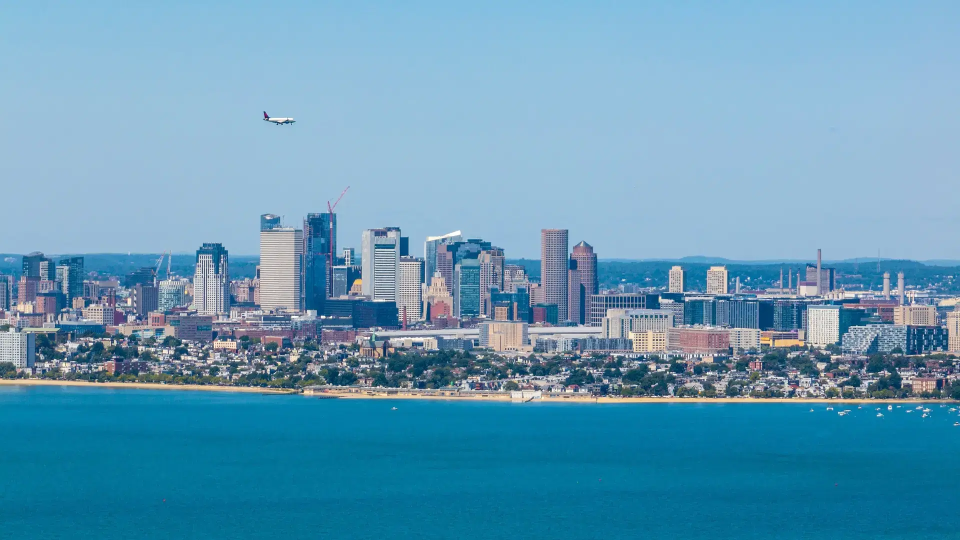 Boston Financial District skyline with a jet landing on Boston Logan Airport viewed from Quincy Bay, Boston, Massachusetts MA, USA.