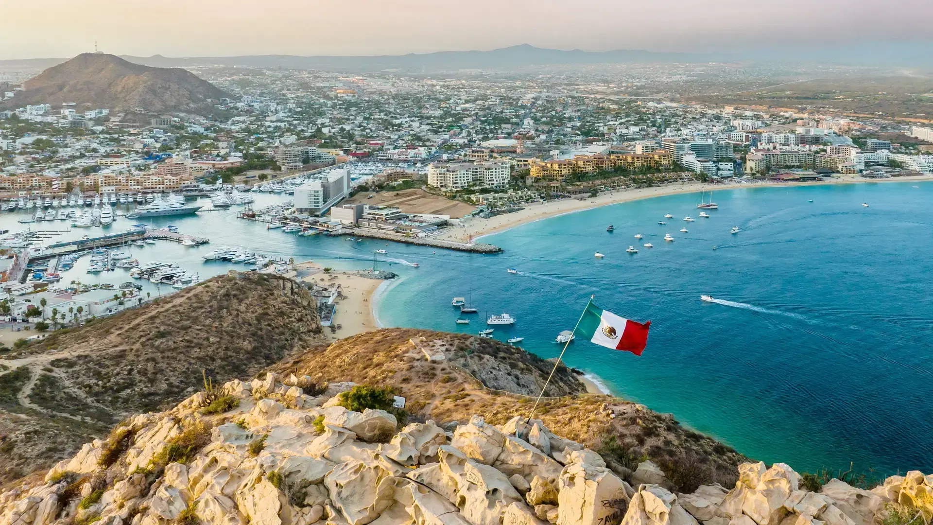 A vibrant flag waving in the foreground of a picturesque cityscape. Cabo San Lucas, Mexico.