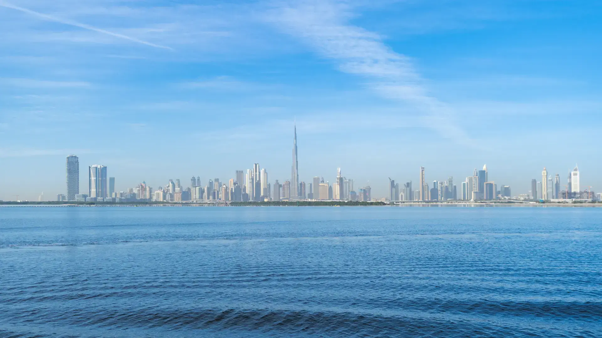 Dubai Downtown skyline with waves on sea beach, United Arab Emirates or UAE. Financial district in travel vacation concept. Urban city. Skyscrapers buildings with blue sky. Reflection