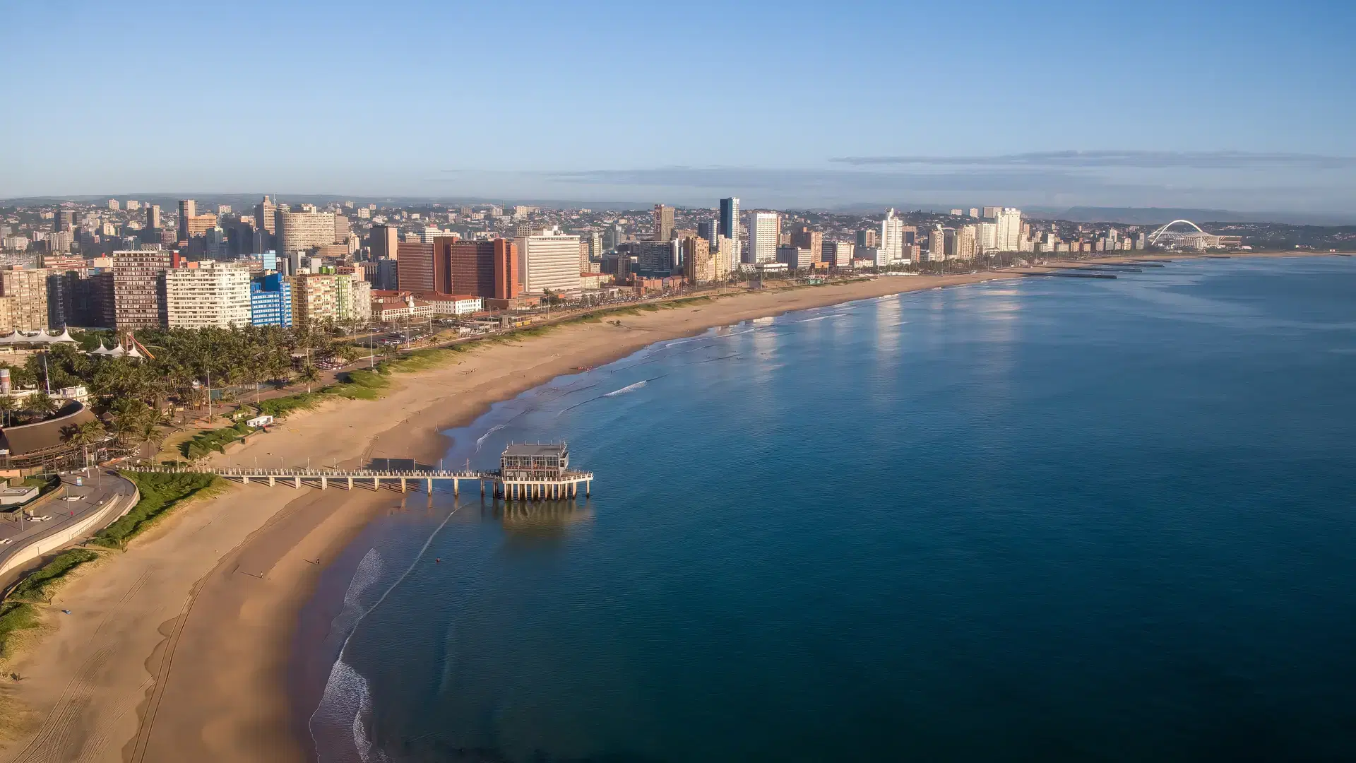An aerial view of the beach, a jetty into the sea, and hotel skyline along Durbans beachfront.