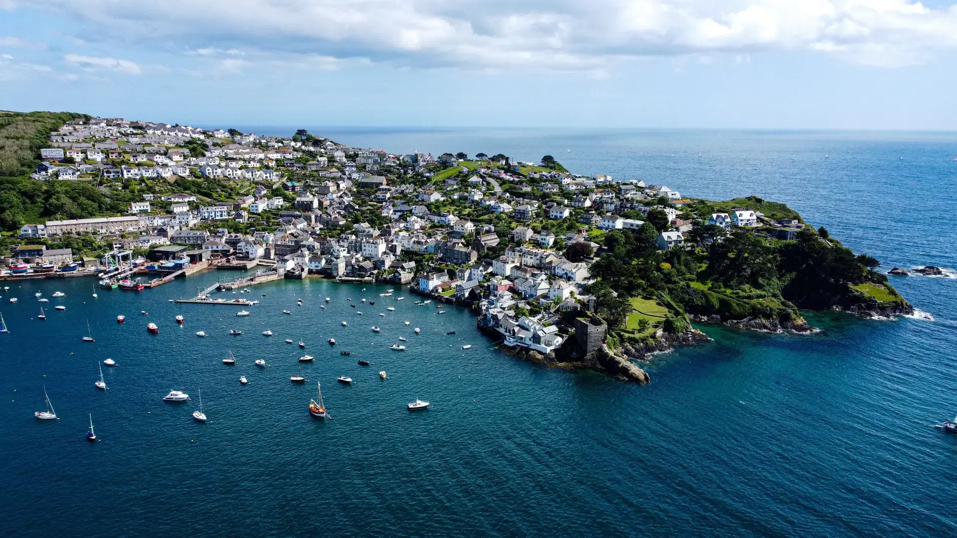 An aerial shot of the Falmouth Cornwall village on the coast of a beach surrounded by hills