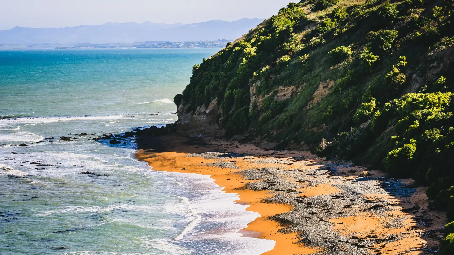 The green slope and orange sand of Bushy Beach, Oamaru, Waitaki District, New Zealand.