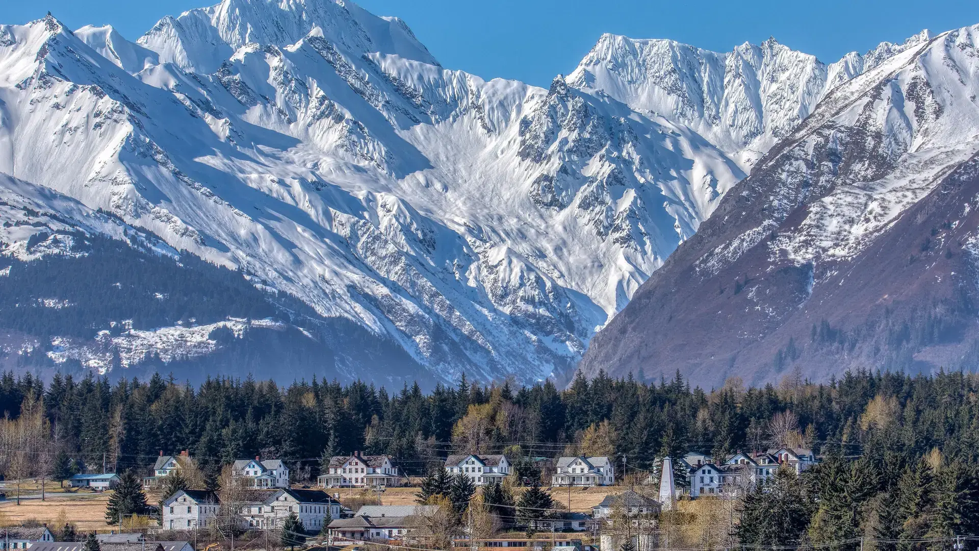 A small houses in rural field surrounded by trees and a snowy mountain in the background in Haines Alaska