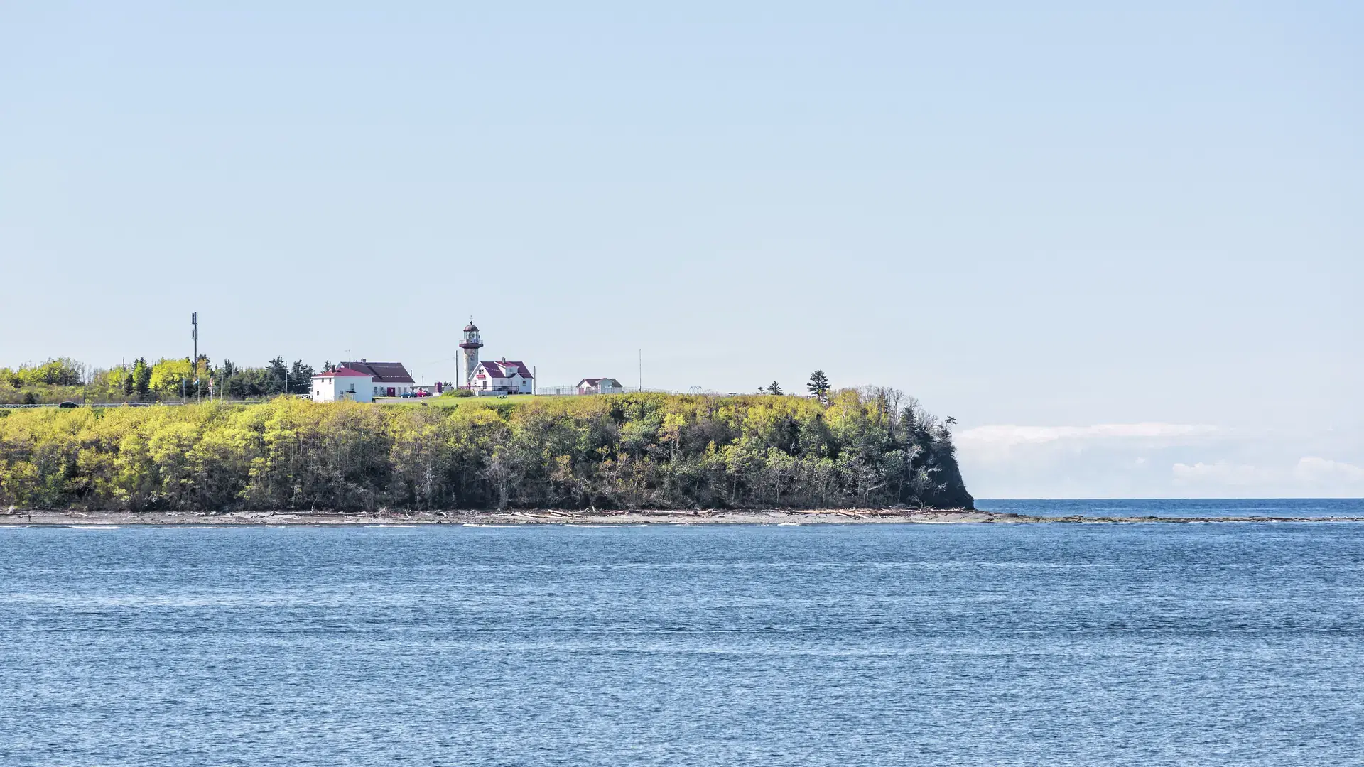 Peninsula coast view of Phare du Cap de Madeleine lighthouse and red painted houses in Saint Lawrence river gulf during day in Gaspe, Quebec, Canada, Gaspesie region