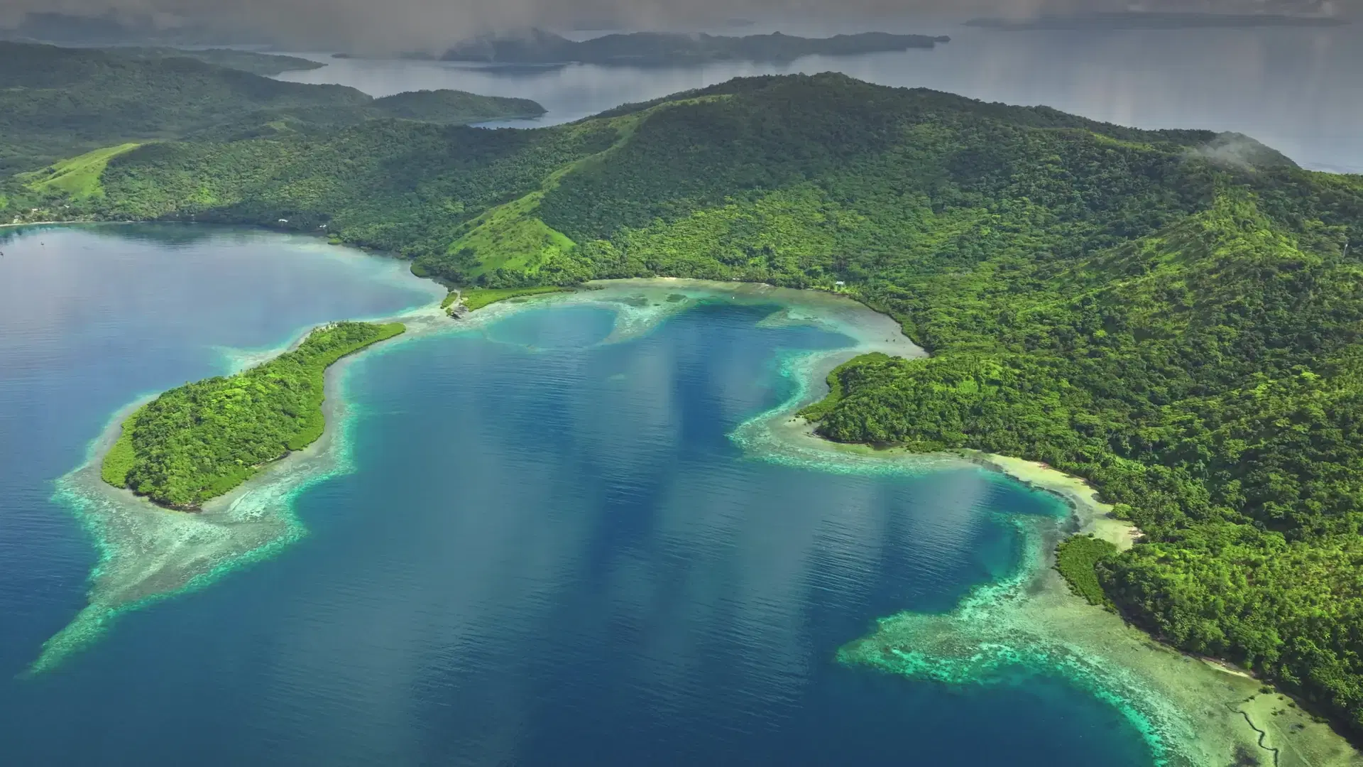 Fiji islands: Aerial view of tropical islands with lush green vegetation reflecting on the turquoise ocean water under a cloudy sky. Wild nature travel landscape. Drone flight