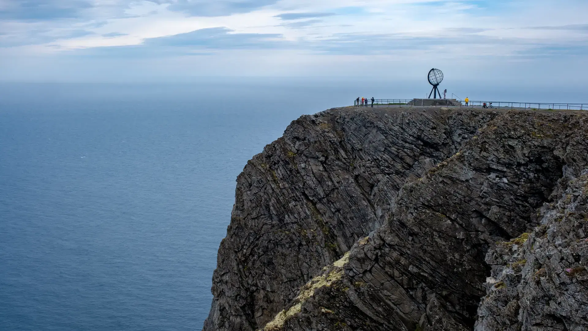 A panoramic view of the rocky cliffs of North Cape in Norway. The iconic globe sculpture stands proudly at the edge of the world, overlooking the vast expanse of the Arctic Ocean.