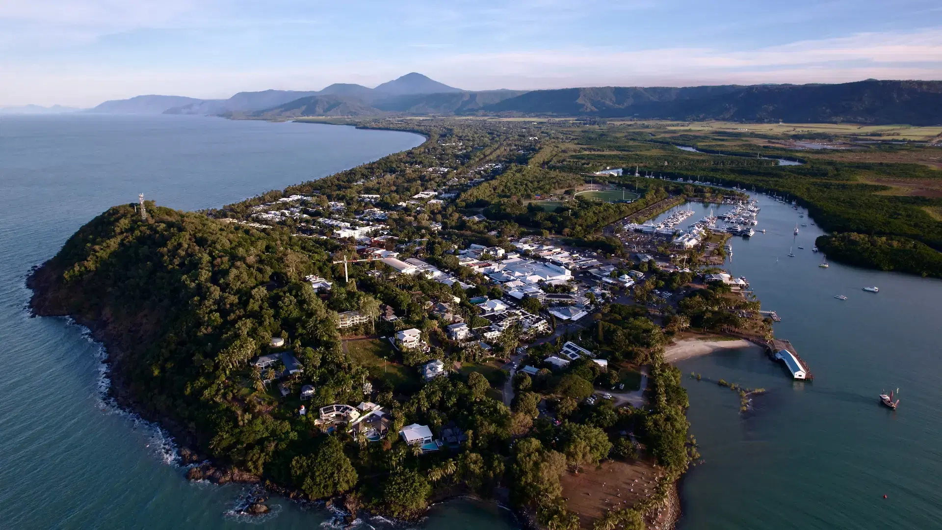 Aerial view of Port Douglas, Queensland, showcasing lush greenery, coastline, and marina under a clear sky.