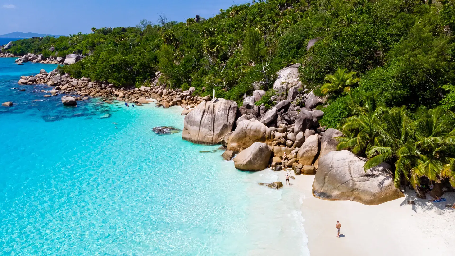 young men on a white beach with turquoise colored ocean, Drone view from above at Anse Lazio beach Praslin Island Seychelles.