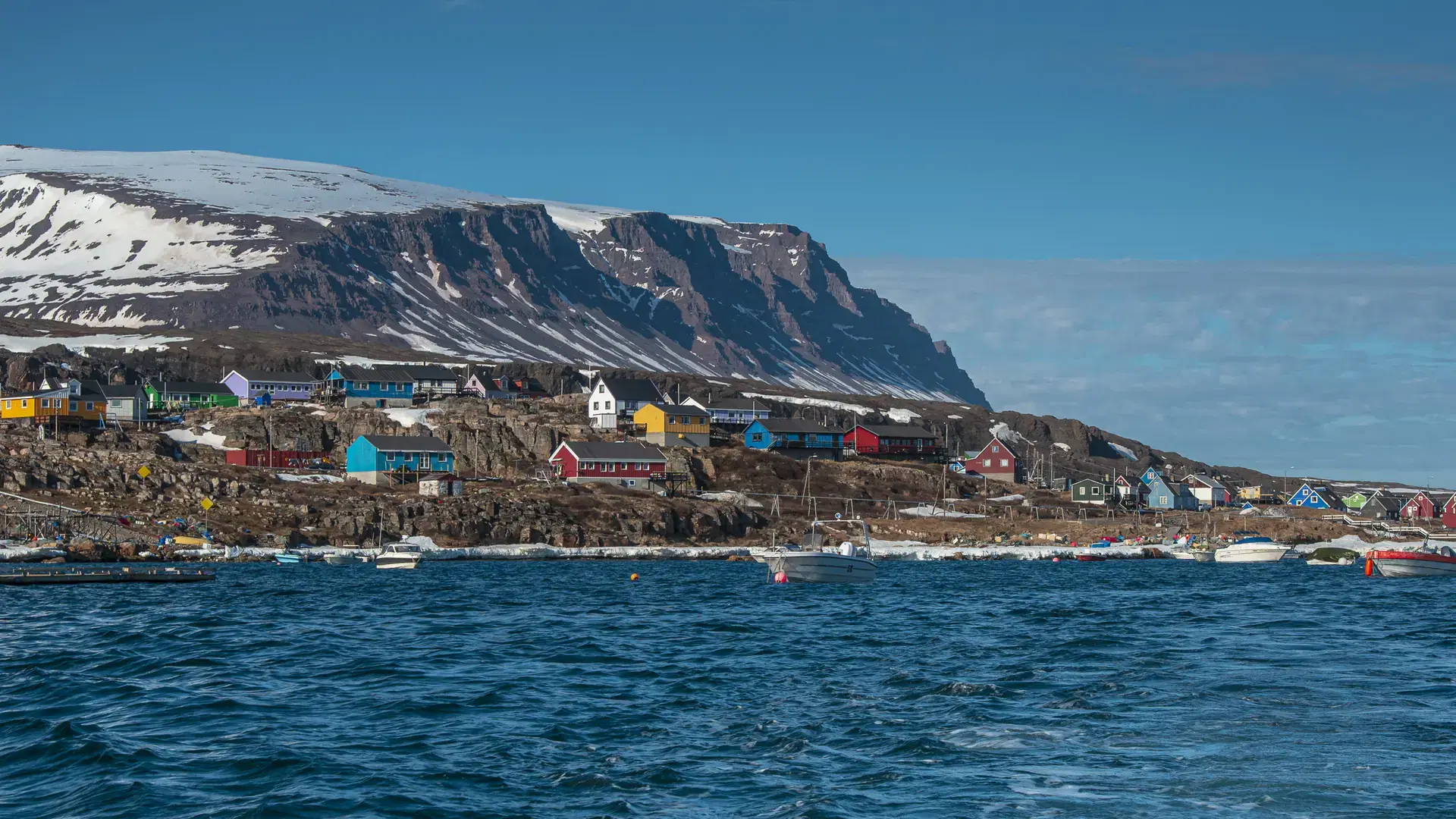 A view of colorful houses near the sea with snowy mountain background at Qeqertarsuaq in Disko Island, Greenland