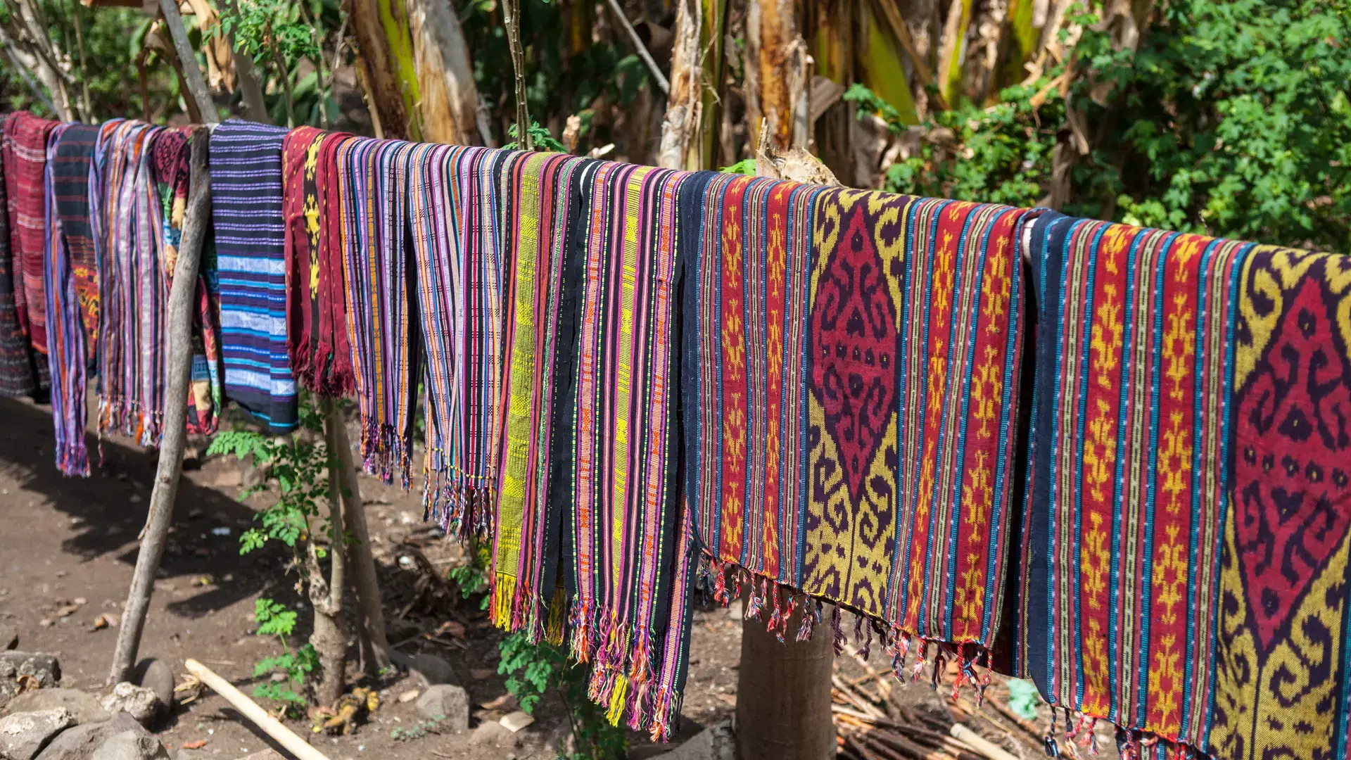 Local, handwoven fabrics hang on a line for tourists to buy on the remote island of Alor, Indonesia. The cotton fabrics are woven and dyed with tribal patterns.