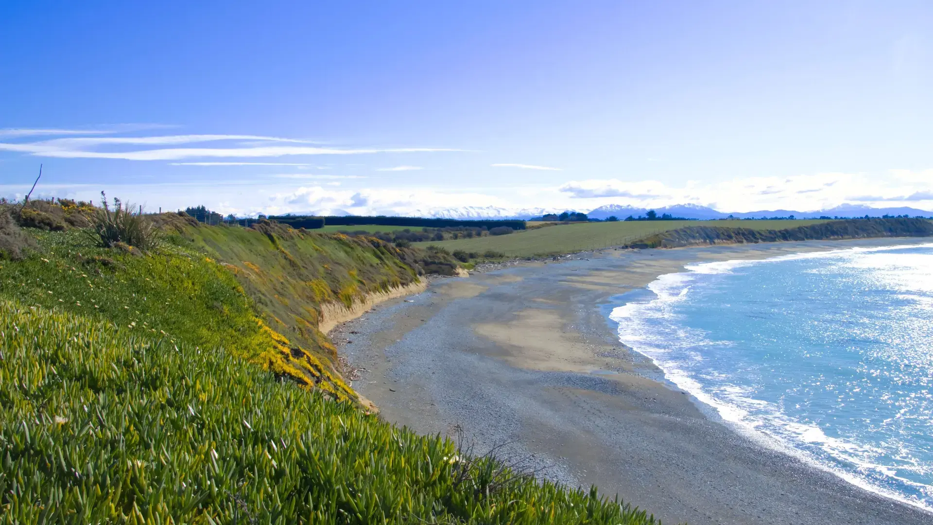 A scenic coastal landscape with a clear blue sky and a sandy beach in Jacks Point, Timaru, New Zealand