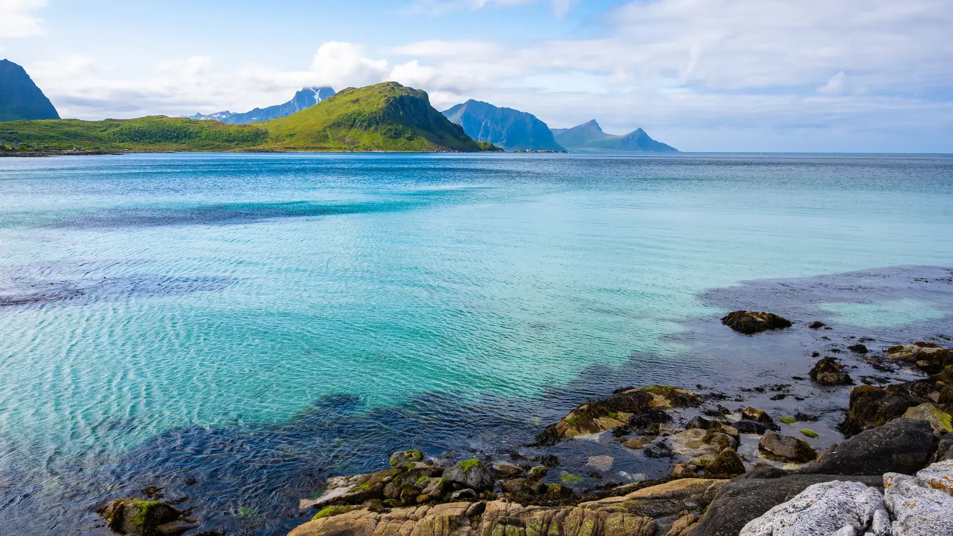 Crystal clear sea water at Vik beach and view of mountains in summer, Lofoten Islands, Norway