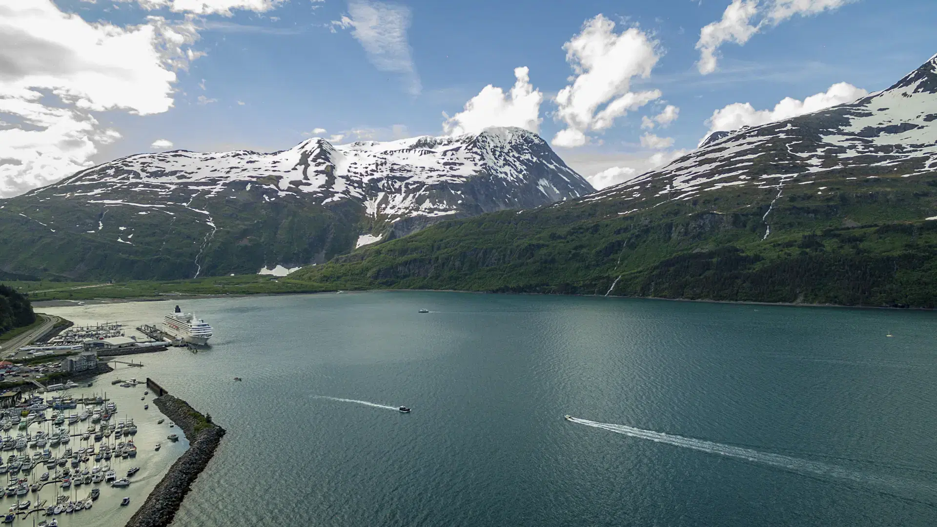 An aerial view of the harbor in Whittier, Alaska, with a cruise ship in the distance
